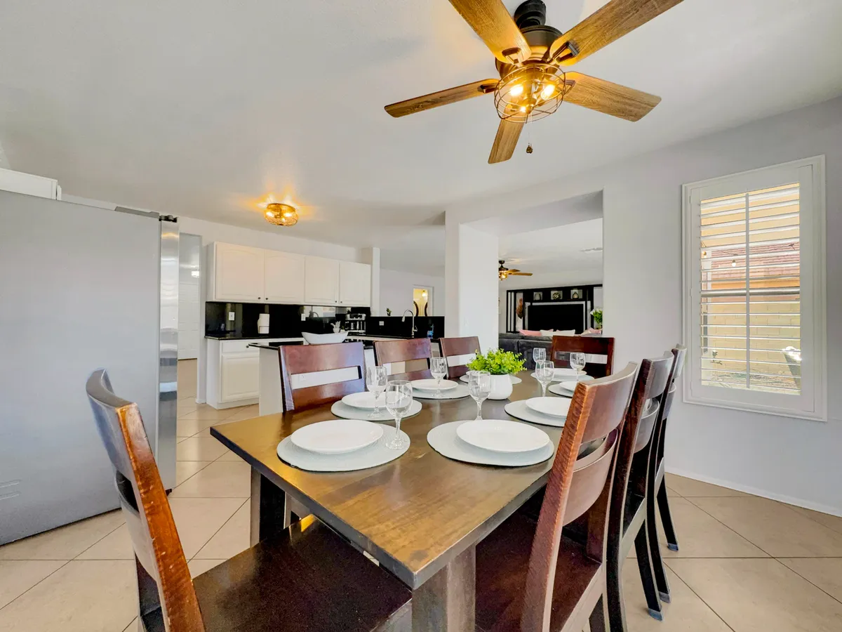 This image features a welcoming interior scene with a dining table set in a spacious area adjacent to the kitchen. The kitchen zone is visible in the background, equipped with modern appliances and generous counter space. The scene exudes warmth, making it easy to imagine both family dinners and lively celebrations occurring here.