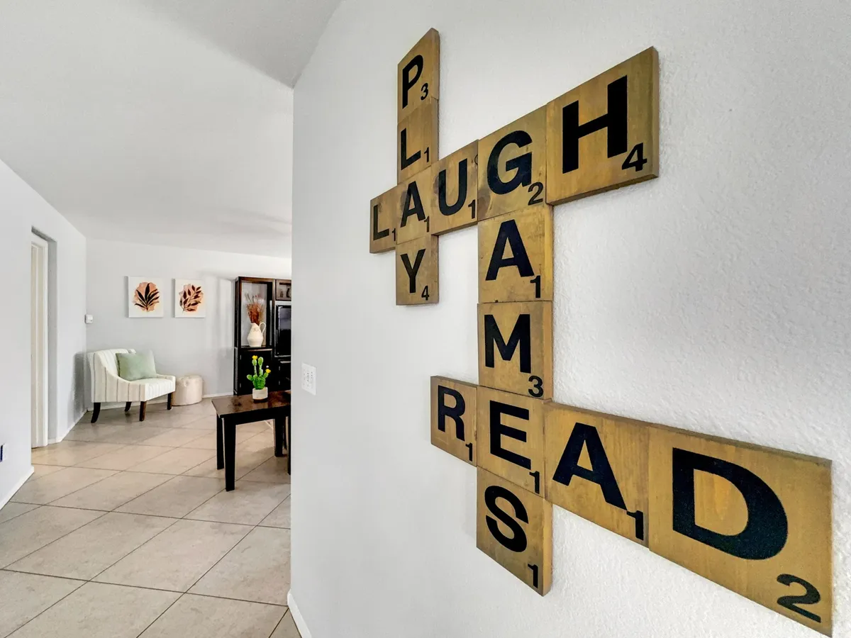 A cozy seating area with a coffee table, surrounded by comfortable chairs. Scrabble-inspired wall art adds a playful, family-friendly touch, while the space is arranged for both group games and relaxed conversation.