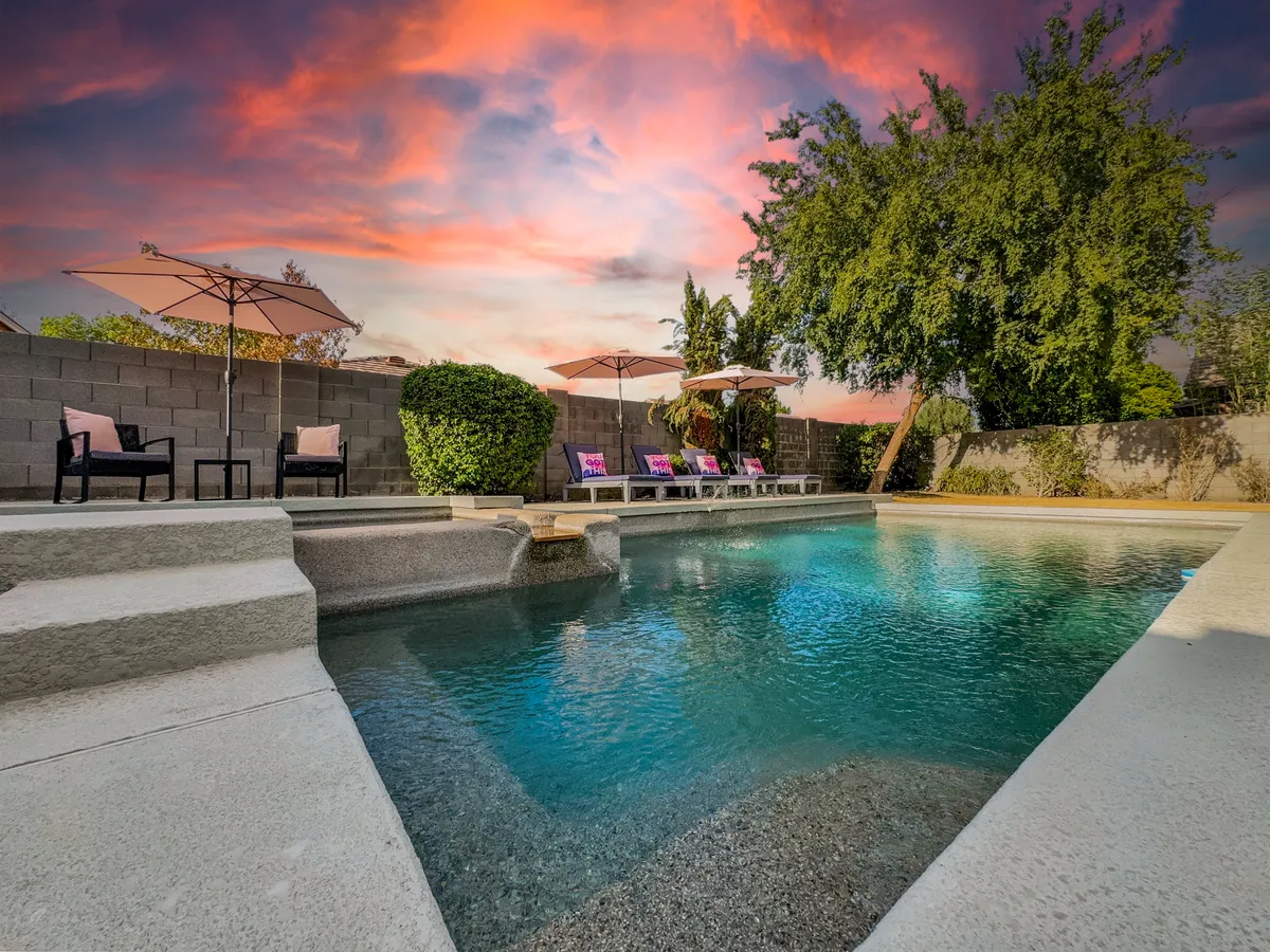 This exterior shot centers on the sparkling swimming pool, surrounded by inviting lounge chairs and umbrellas, all set within lush, landscaped greenery. The space is staged for relaxation, sunbathing, swimming, and socializing in a resort-style environment.