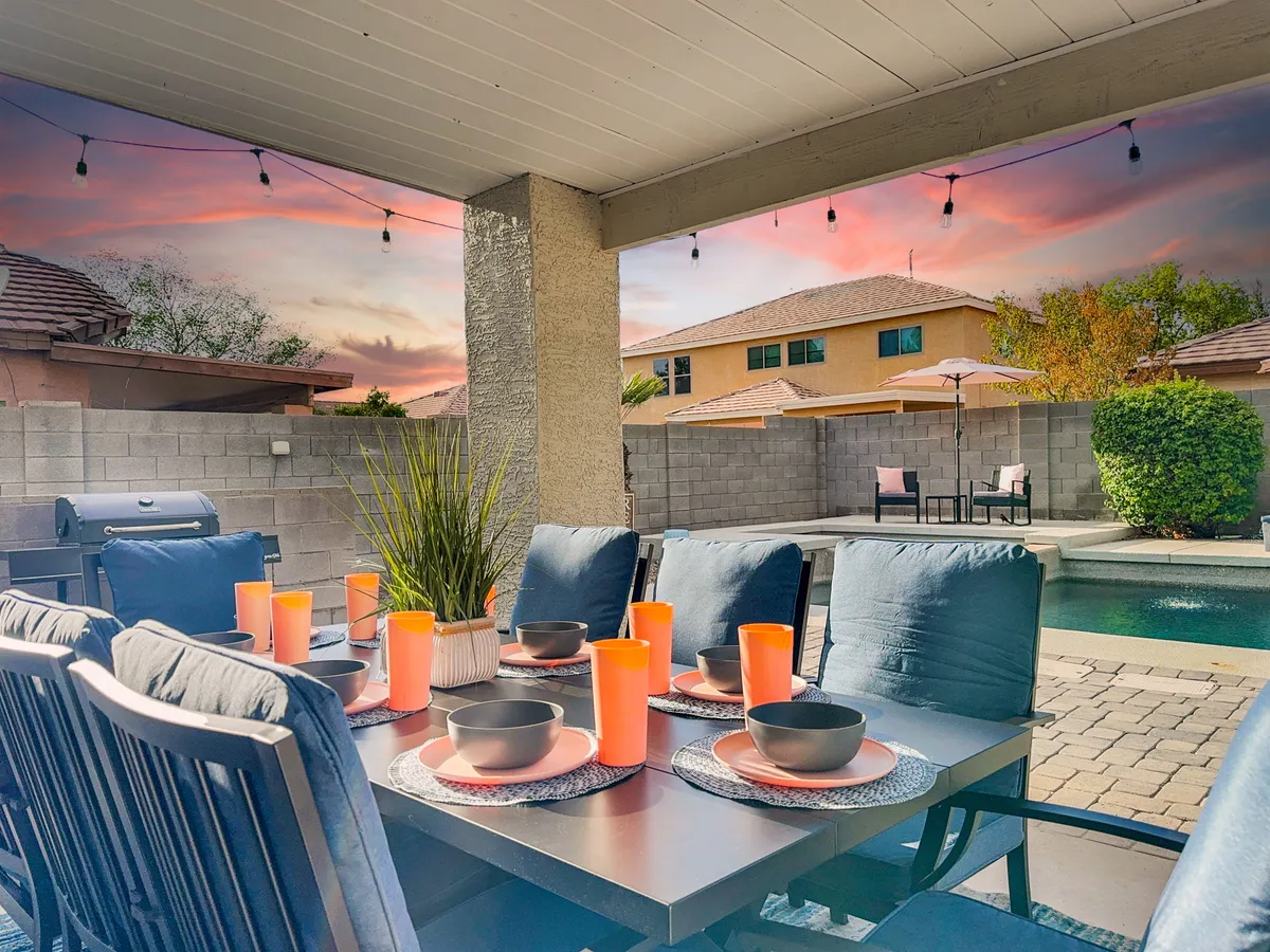 A cheerful outdoor dining setup featuring a table with plates and glasses, a swimming pool in the background, and string lights above. The ambiance is festive and relaxed, hinting at celebrations or casual gatherings with friends and family.