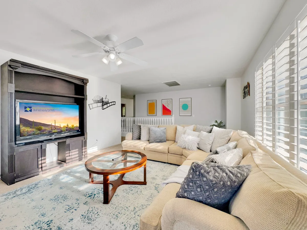 A large sectional sofa set around a coffee table, with a TV stand and television, abstract artwork on the walls, and decorative throw pillows. The space is filled with warm lighting and inviting decor, emphasizing comfort and togetherness.