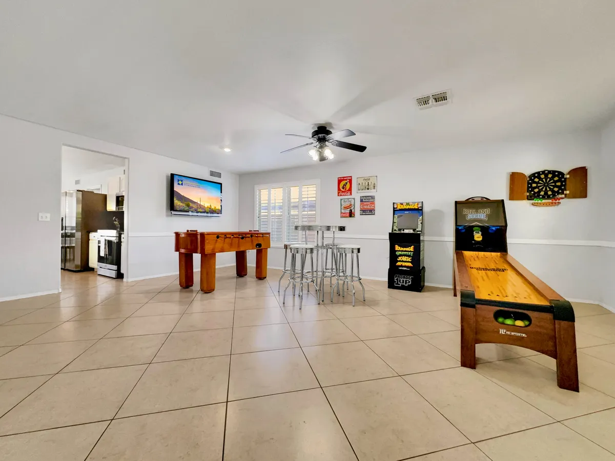A dynamic game room scene with a foosball table, dartboard, skee-ball machine, a set of stools, and a television. The lively setup invites group play, celebration, and togetherness, echoing the festive mood of family gatherings and get-togethers.