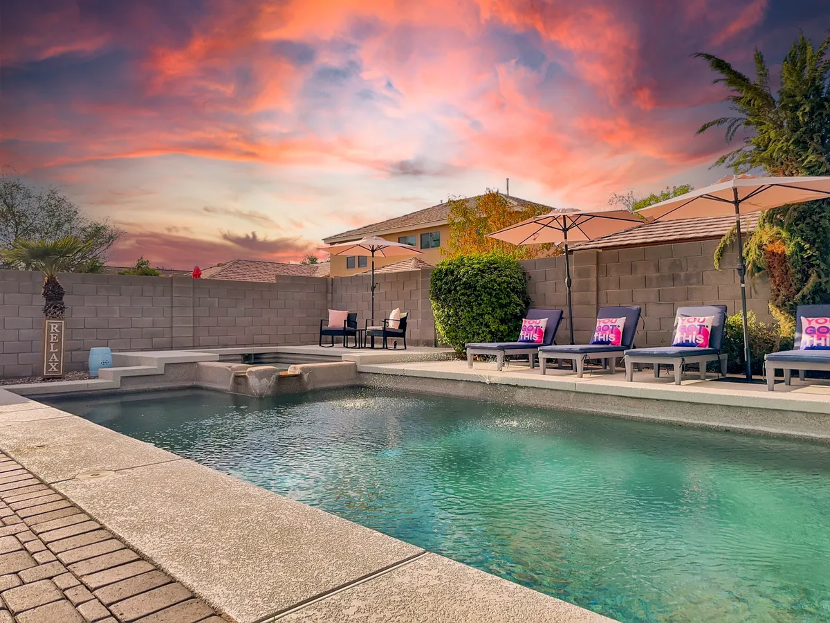 A vibrant exterior photo featuring a glistening swimming pool, ample lounge chairs under umbrellas, and an expansive sky. The scene is set for group relaxation, pool parties, or quiet escapes, emphasizing spaciousness and luxury.