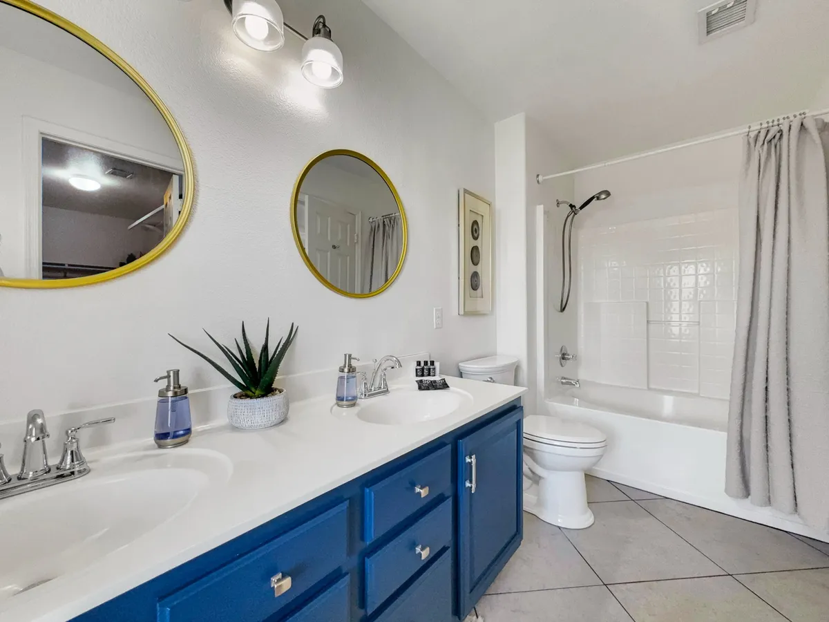 A bright, refreshing bathroom space featuring a double vanity with blue cabinetry, mirrors, and a bathtub. The ambiance is calm, inviting, and ideal for relaxation or rejuvenating routines.