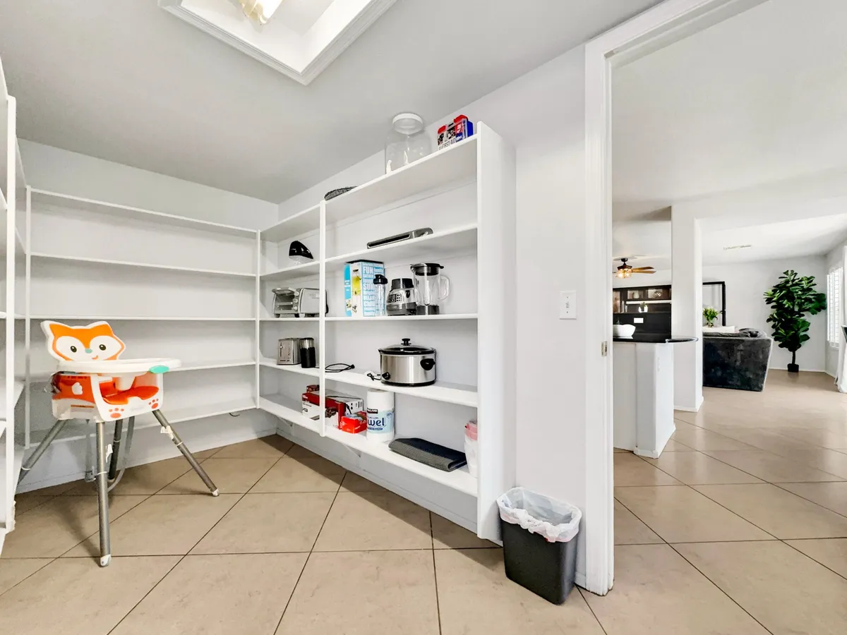 An interior view of a functional and family-oriented kitchen area, featuring a high chair with a fox design, open shelving stocked with kitchenware, and visible kitchen appliances. The space is designed for group meal prep and casual family gatherings.