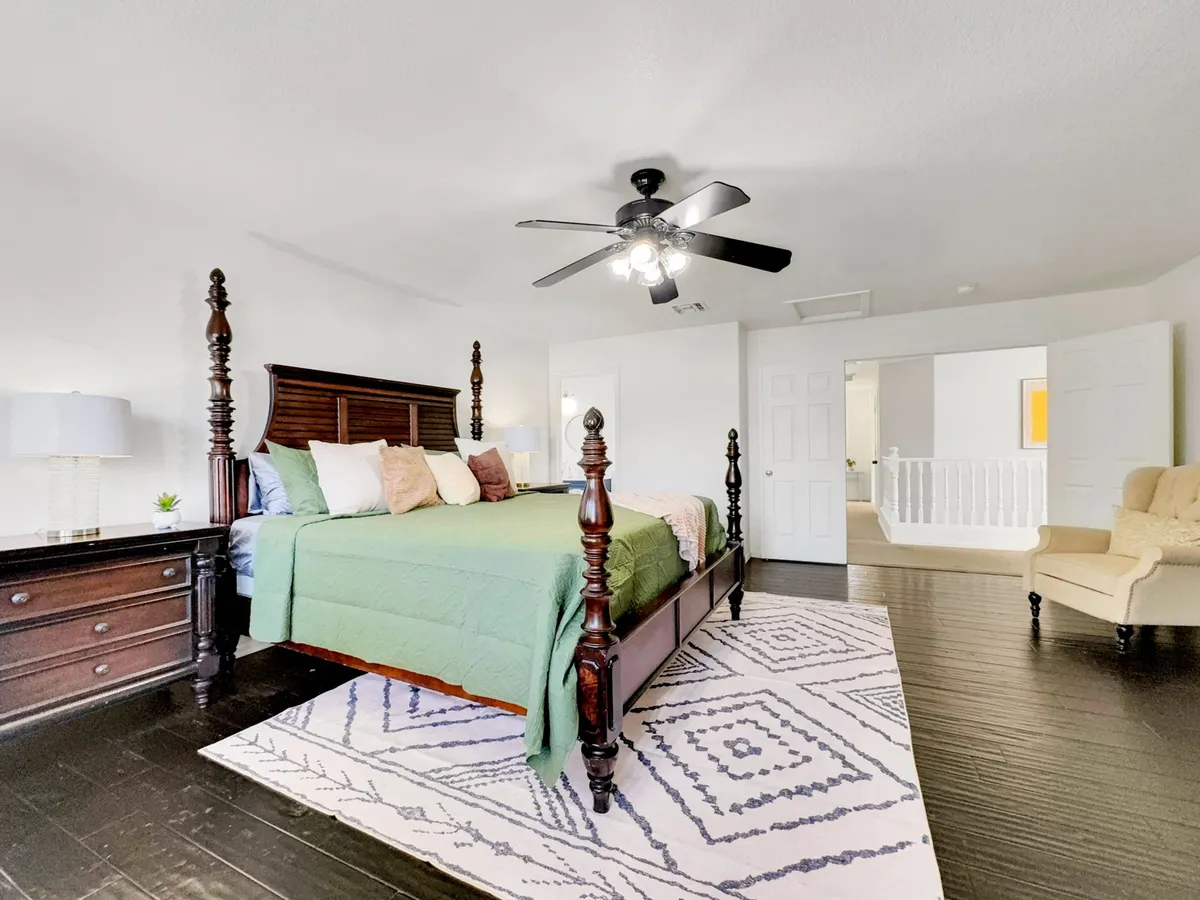 A serene interior featuring a four-poster bed adorned with decorative pillows, an area rug, and a nightstand with a lamp. The room is softly lit with natural light, creating a tranquil and inviting atmosphere ideal for relaxation.