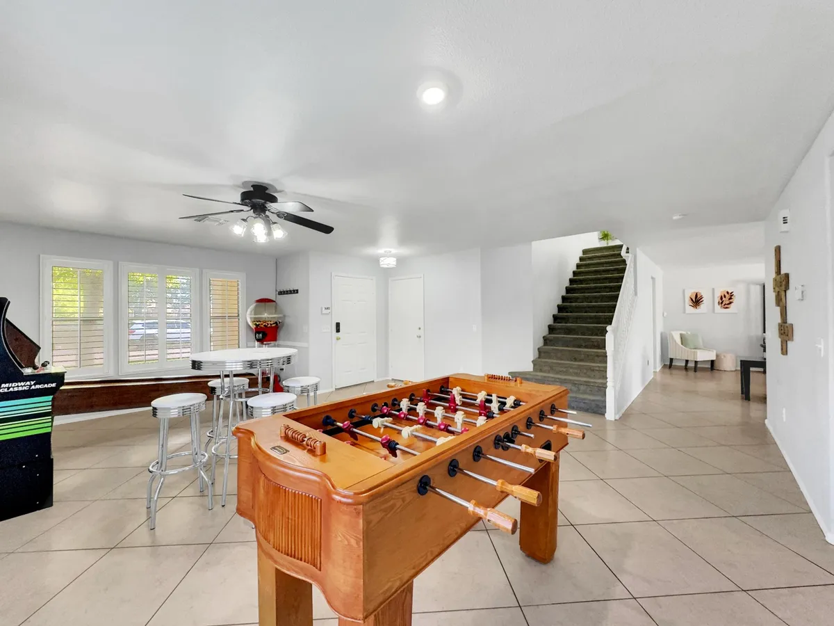 A stylish interior shot emphasizing the foosball table in the foreground, with an arcade game, bar stools, and a cozy seating area nearby. The room is designed for recreation and socializing, encouraging casual hangouts and active play.